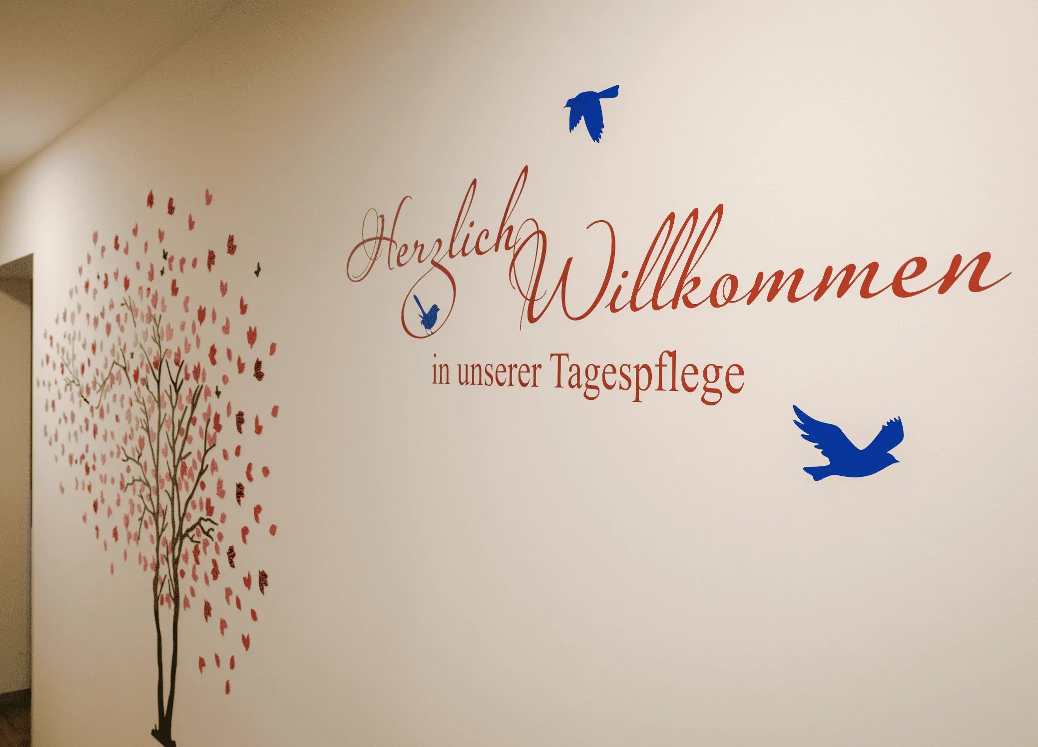 Wandbemalung mit Baum, Vögeln und dem Schriftzug „Herzlich Willkommen in unserer Tagespflege“ bei Silenza